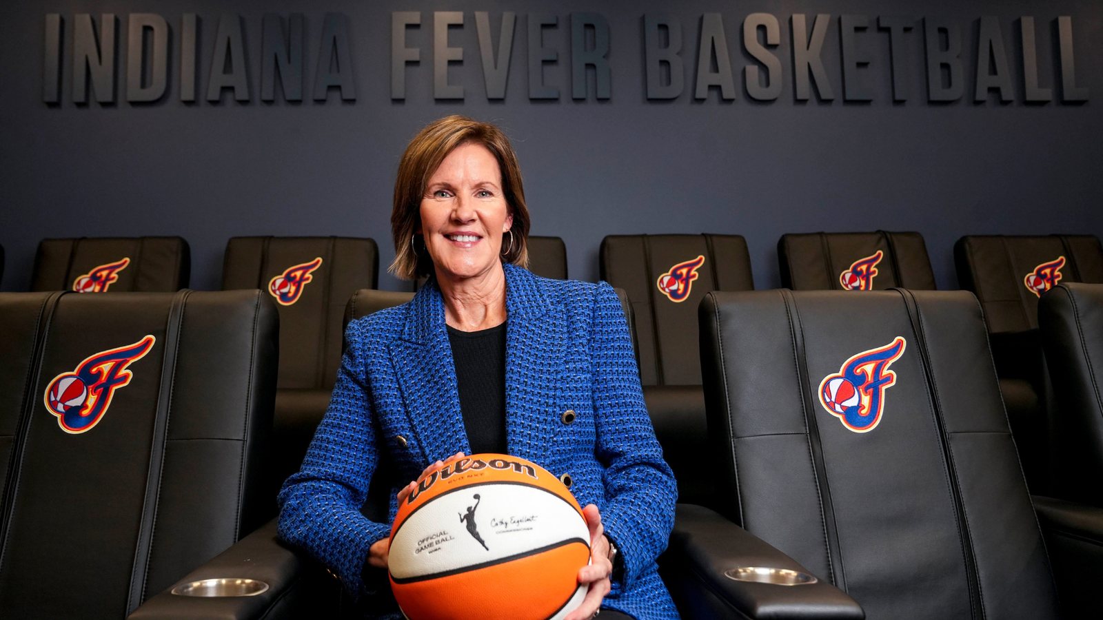 Kelly Krauskopf sits holding a basketball in front of Indiana Fever seats.