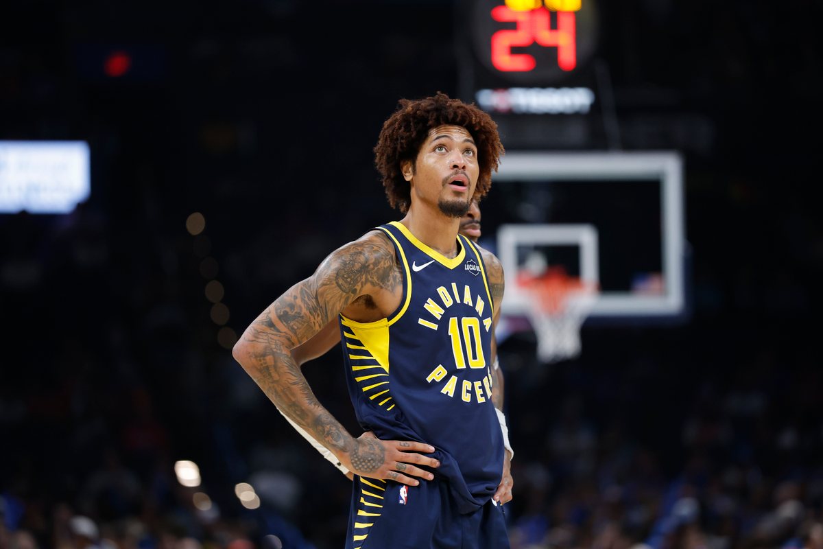Kelly Oubre Jr., hand on hip in a navy Pacers jersey, looks up at the video board in Oklahoma City.