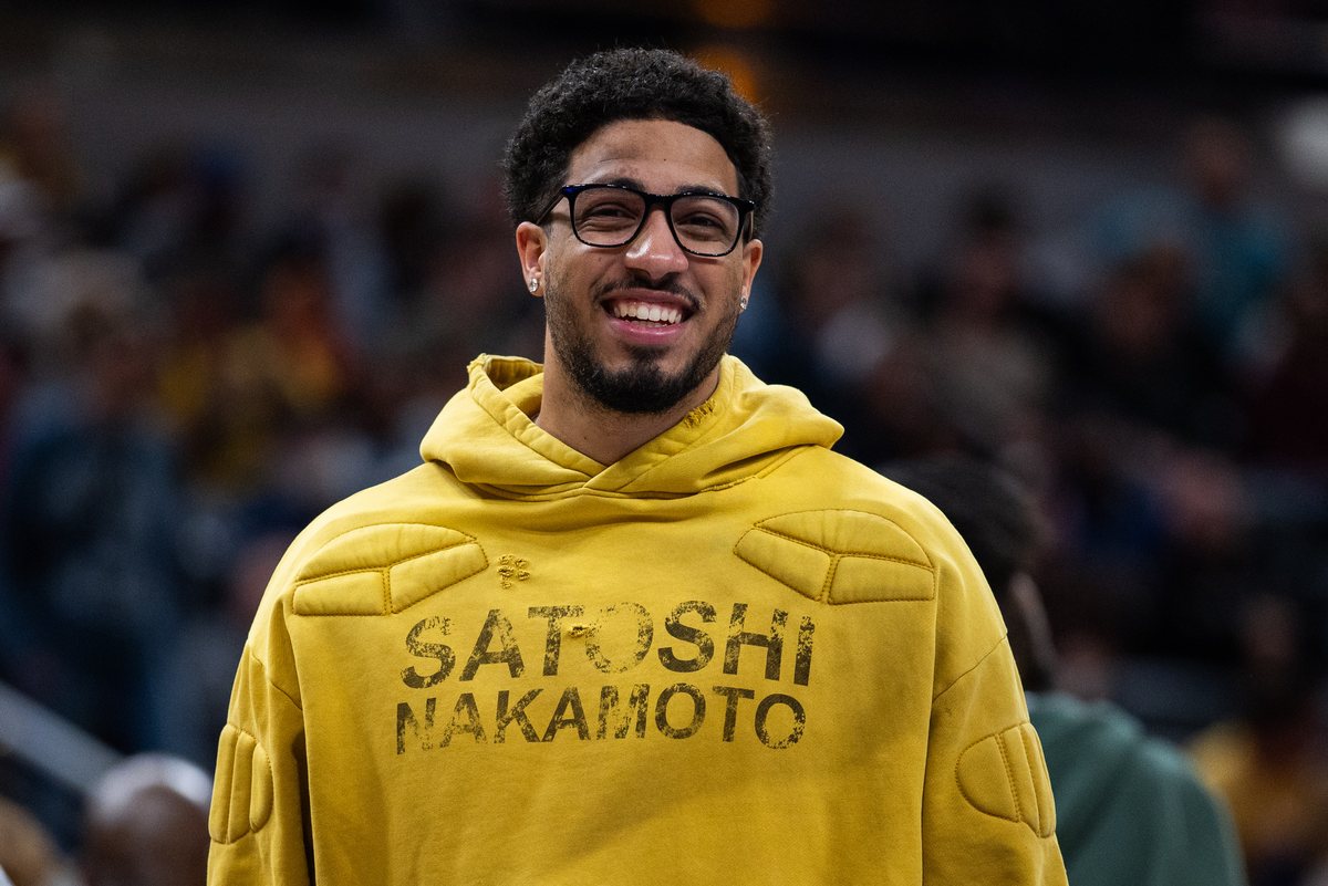 Tyrese Haliburton, wearing glasses and a yellow hooded sweatshirt, smiles on the sideline at Gainbridge Fieldhouse.
